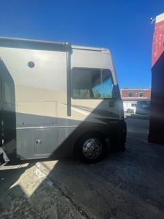 Side view of a beige and black RV parked outdoors with a window and a black wheel visible.