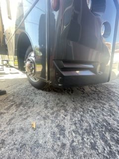 Dark colored bus, parked on asphalt; front side with wheel and steps.