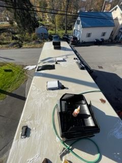 A person cleaning the roof of a white RV with a green hose, outside.