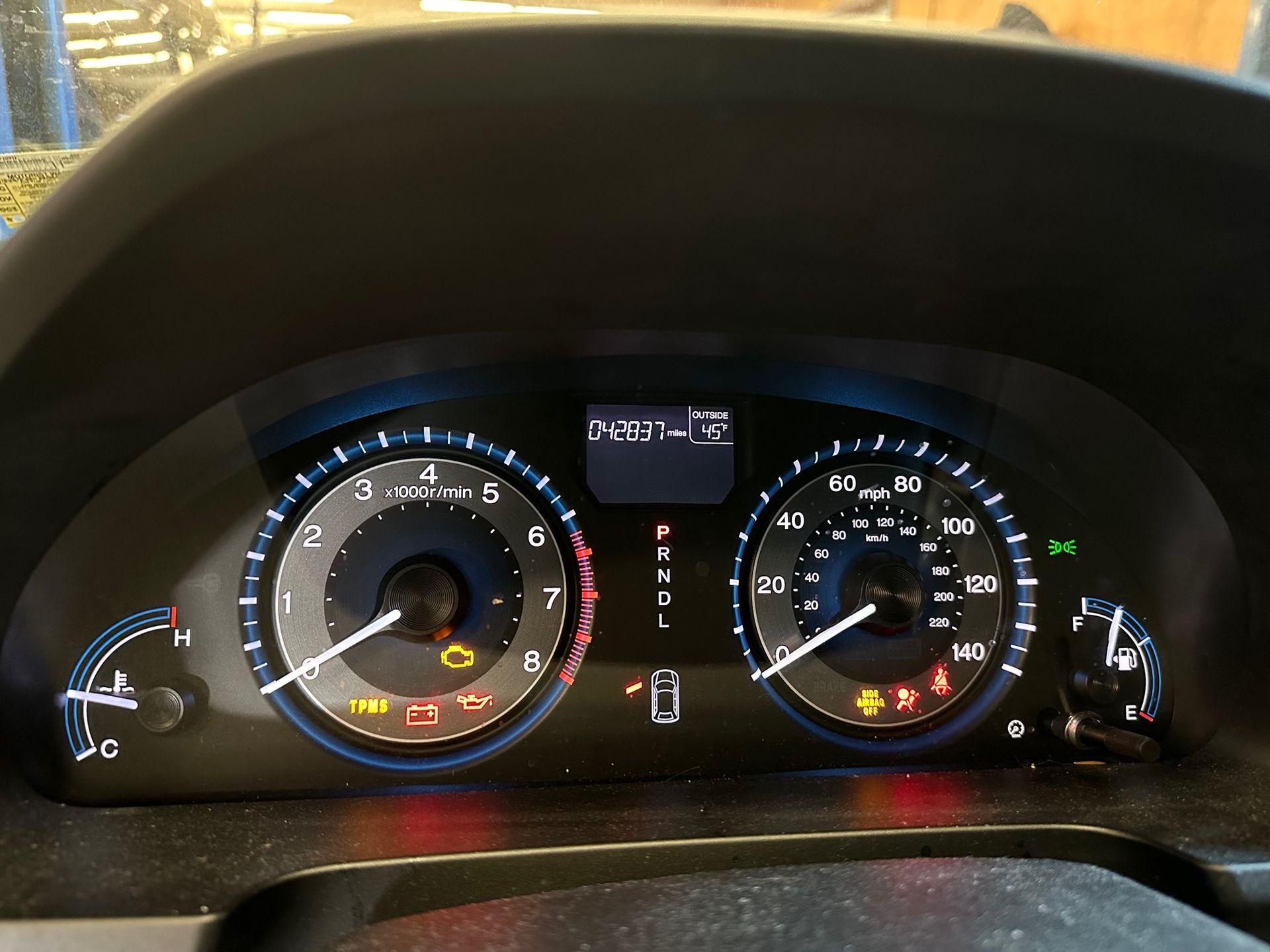 Car dashboard with illuminated warning lights; speedometer and tachometer visible.
