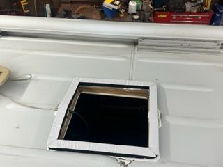 A square black window cut into a white vehicle roof, framed by cardboard and mounted with sealant.