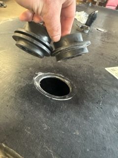 Hand holding two black rubber grommets next to a hole in a dark surface.