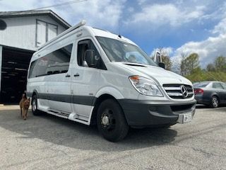 White Mercedes-Benz Sprinter van parked in front of a building; dog nearby.