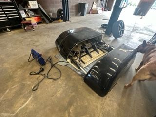 Black grill parts on a concrete floor with a dog nearby and a glue gun. Garage setting.