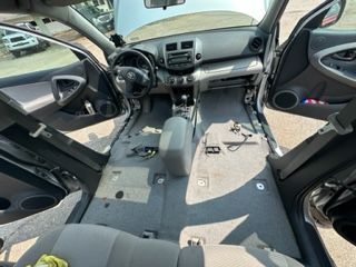 Interior view of a black Toyota RAV4 with seats and carpeting removed, doors and hood open.