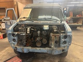 A light blue van with the hood open, revealing the engine. The van is in a garage.