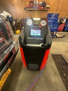 Snap-on AC recovery machine in a garage setting with car and tools visible.