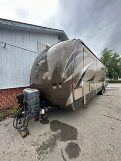 Tan and brown travel trailer parked in front of a building on a cloudy day.