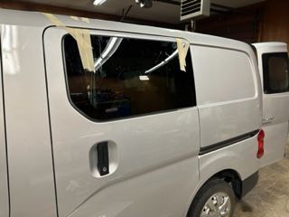 Silver van with tinted window, taped in place, in a garage.