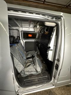 Interior of a silver van, showing rear seats, a barrier, and open side door.