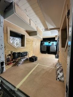 Interior of a van under construction. Wooden walls, flooring, cabinets, and wiring are visible.