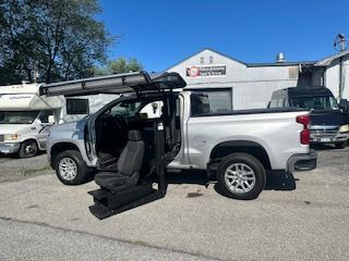 Silver pickup truck with a door modification for wheelchair accessibility in front of a building.