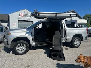 Silver pickup truck with accessible lift, open door revealing a black seat, ramp extended.