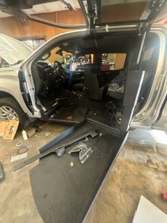 A silver truck's interior gutted; ramp extended; garage setting.