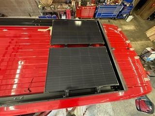 Two black solar panels installed on a red vehicle roof. Workshop setting.