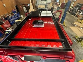 Red van roof with a black rack, equipment and a vent in a workshop.