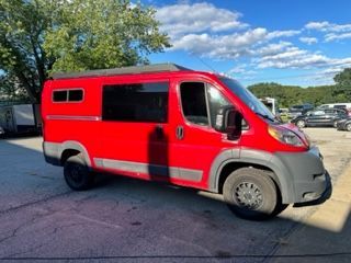 Red camper van with black tires parked outside under a bright sky.