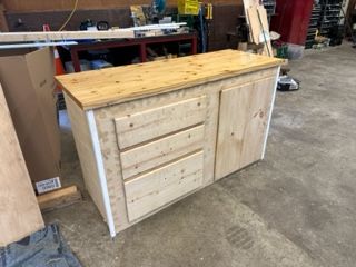 Light wood cabinet with drawers and door in a workshop setting.