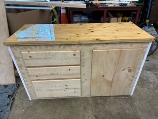 Wooden cabinet with drawers and a door, constructed with light-colored wood, white trim, and a blue-painted top section.