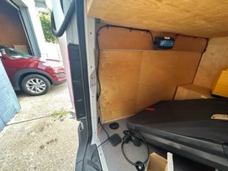 Inside of a van: wooden shelving and a black case, door open showing a red car.