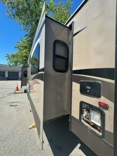 Side view of a tan RV with a slide-out extended; parked on asphalt, blue sky.