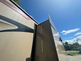 RV side with a slide-out extended, beige and brown colors under a blue sky.