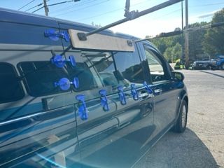 Dark van with blue suction cups attached to the side window, sunlight, outdoors.