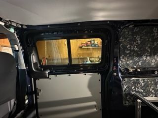 Interior of a van with installed window, insulated walls, and metal panels.