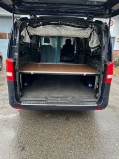 Back of a blue van with the door open, showing a bed frame built inside.