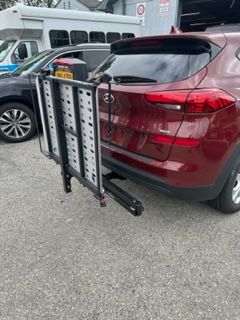 Red SUV with a black wheelchair carrier attached to the back, parked on pavement.