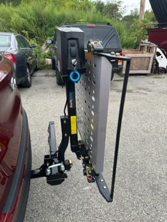 A wheelchair lift attached to the back of a red car in a parking lot.