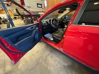 Red car interior, driver's side door open, showing black seats, steering wheel, and dashboard.