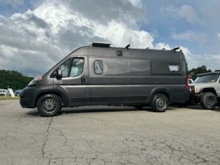 Gray camper van parked on asphalt, cloudy sky.