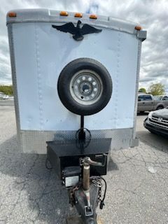 White cargo trailer with a spare tire mounted on the front. A black eagle emblem is above.