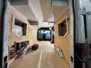 Interior of a van being converted, with wood paneling, windows, and electrical components visible.