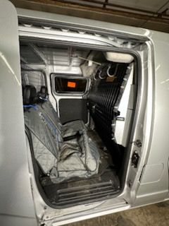 Interior of a silver van with open side door. Seats covered in protective material. Interior with safety divider.