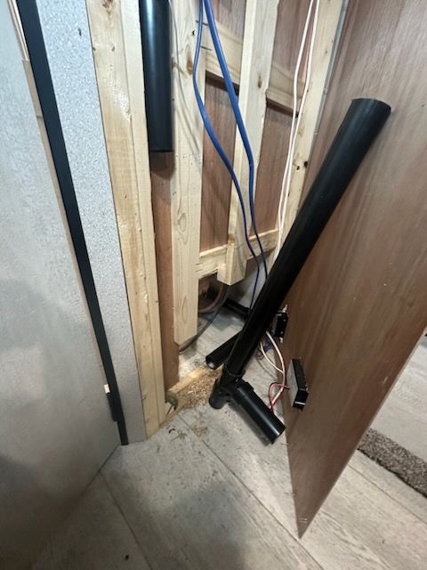 Wooden framing with exposed wires and black pipes near a partially open door.