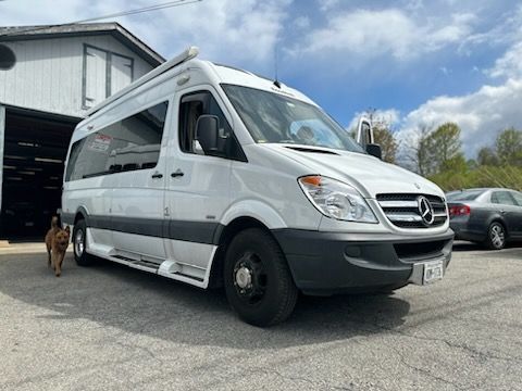White Mercedes Sprinter van parked outside a building. Dog runs by.