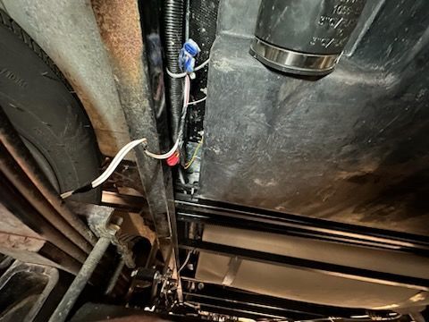 Underneath a vehicle, black tank, wiring, and pipes are visible.