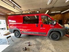 Red van parked in a garage with black tires and tinted window. Tools on the floor.