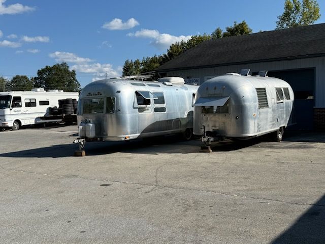 Two silver Airstream trailers parked outside a building on a sunny day.
