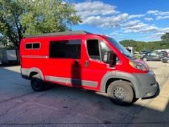 Red camper van with black accents parked outdoors under a blue sky.