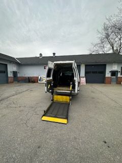 White accessible van with lowered ramp in front of a gray building. The ramp is yellow and black.