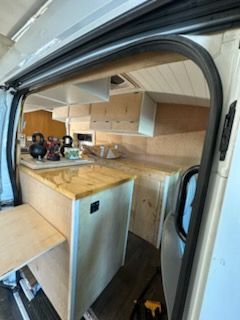 Interior of a van converted into a camper with wooden cabinets, countertops, and a fold-out table.