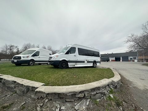 Two white vans parked on grass near a building under an overcast sky.