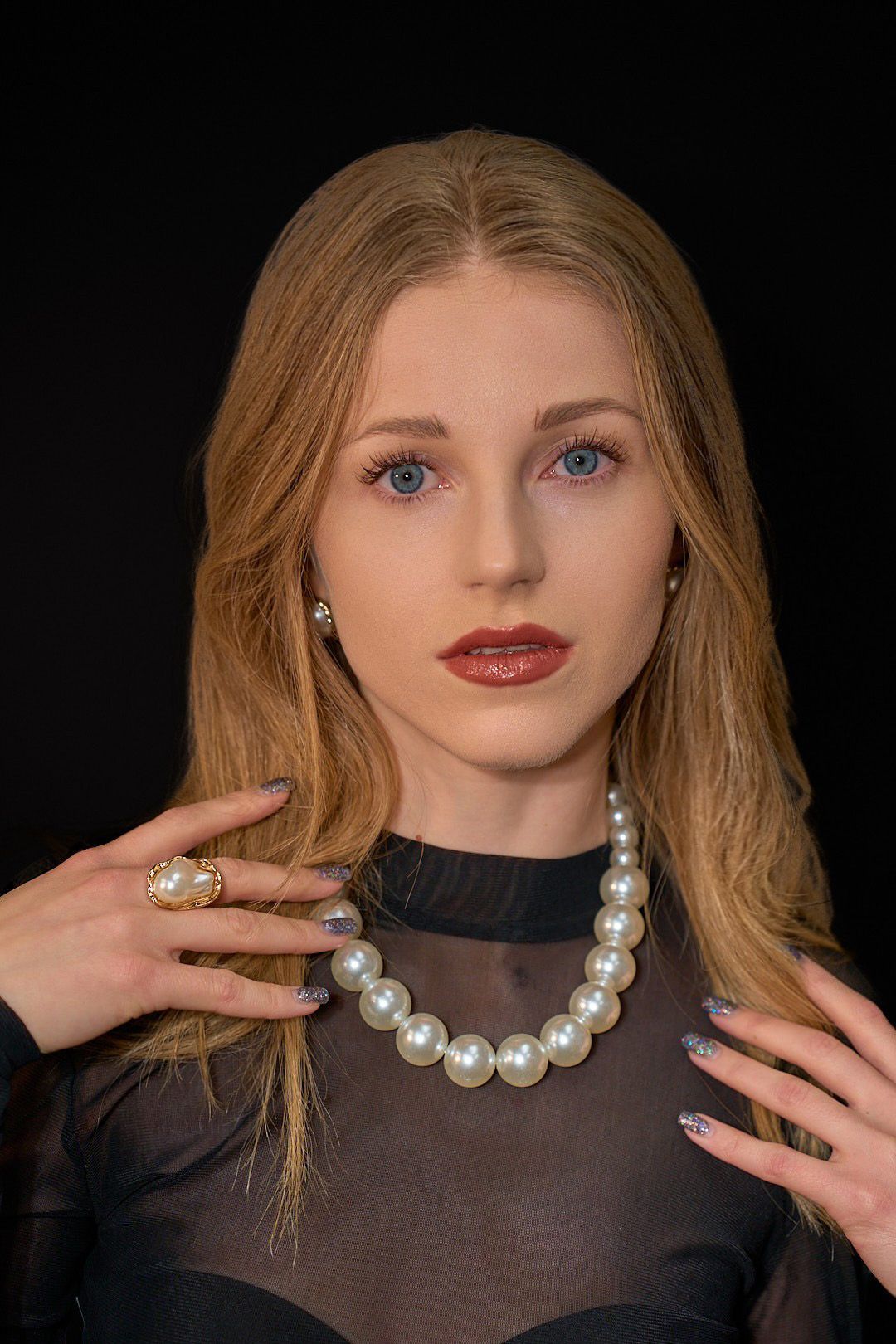A woman is wearing a pearl necklace and a ring.