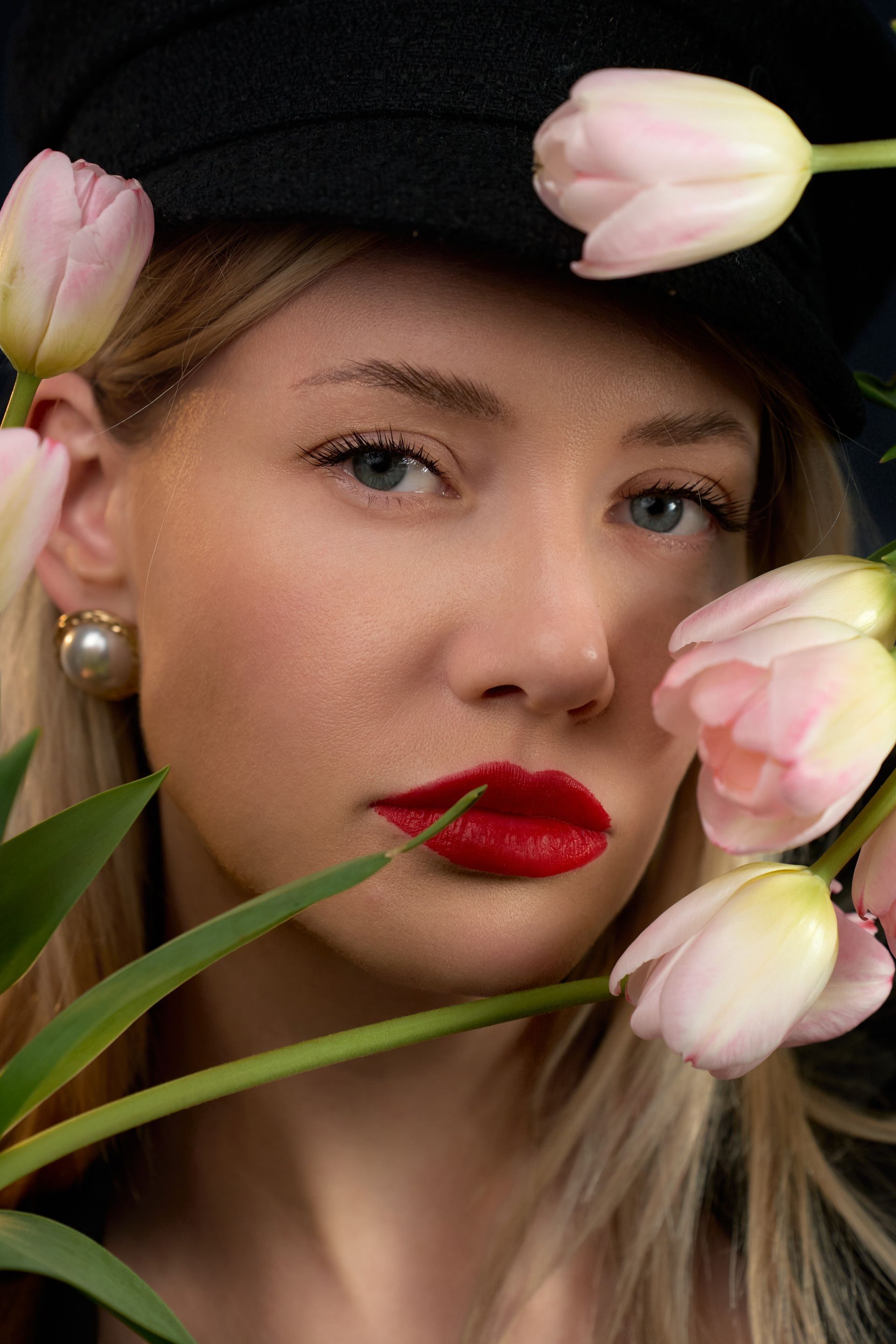 A woman wearing a hat and red lipstick is holding flowers in front of her face.