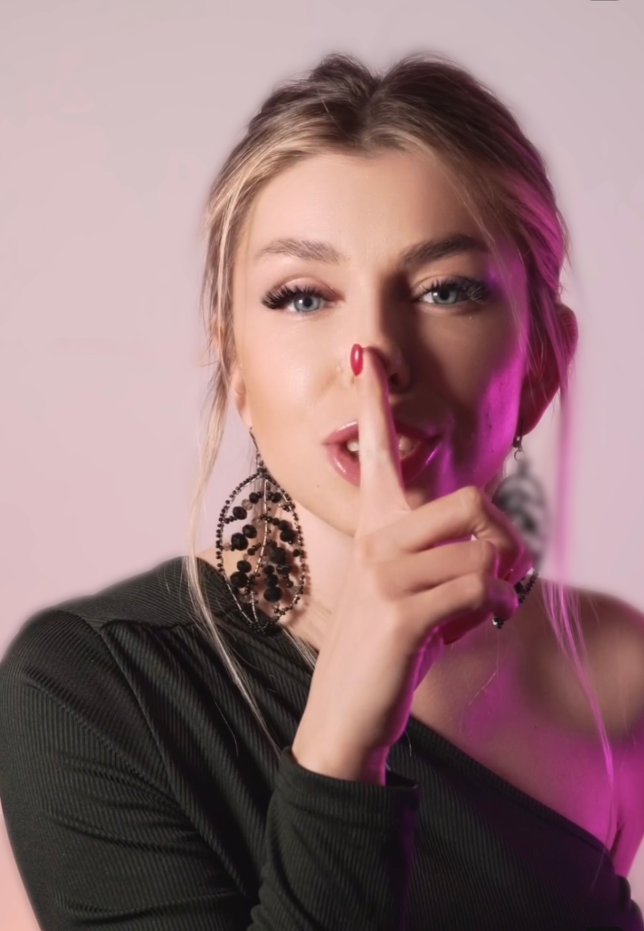A woman is holding her finger to her mouth while wearing earrings.