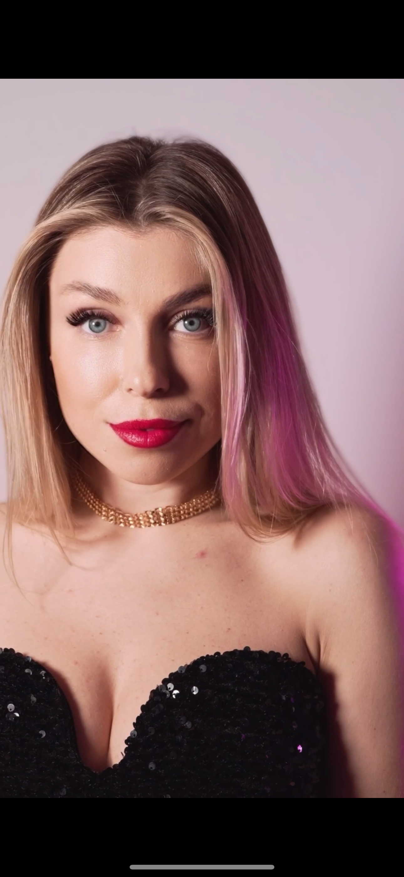 The woman is wearing a black dress and a gold necklace.