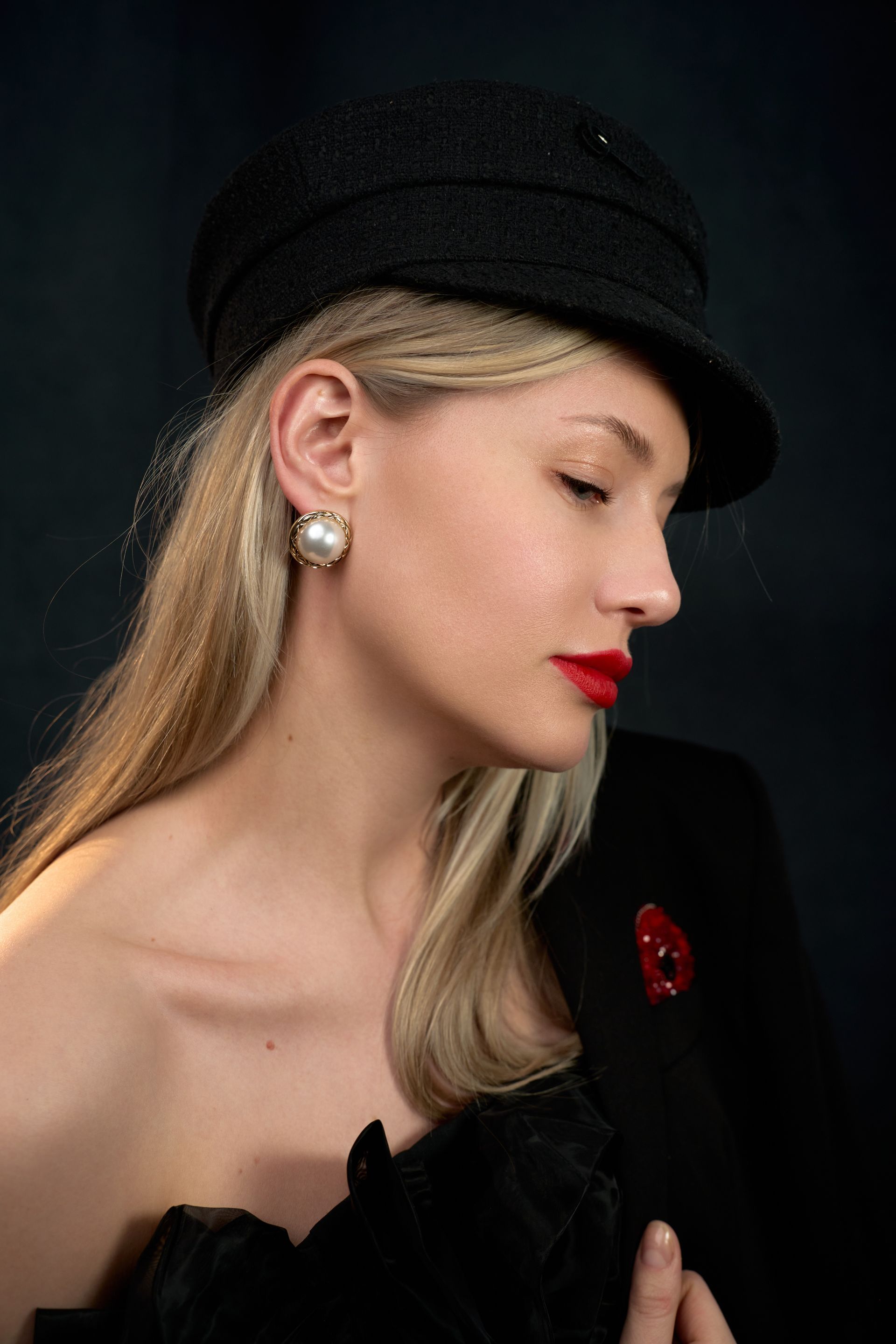 A woman wearing a black hat and red lipstick is looking down.